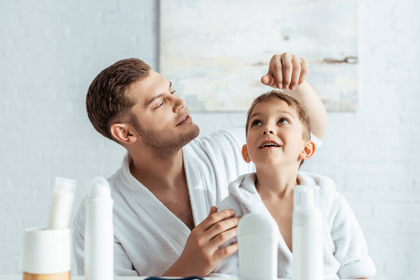 selective focus of young father touching hair of cheerful son near toiletries in bathroom - Photo, Image