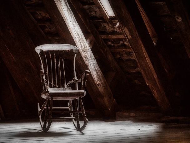 Vecchia sedia a dondolo in legno su una soffitta con un fascio di luce attraverso una finestra - Foto, immagini