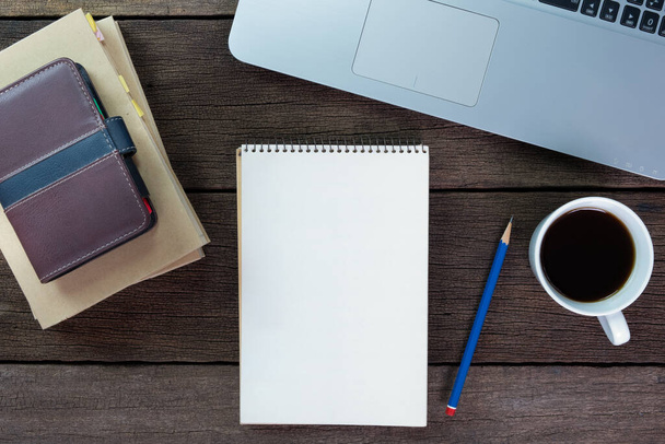 Carnet blanc vierge avec crayon, café, ordinateur portable, organisateur et livre sur bureau en bois, vue sur le dessus. - Photo, image