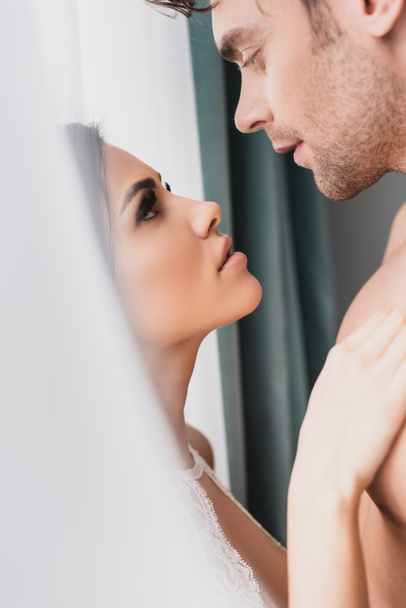 Selective focus of beautiful woman touching chest of muscular boyfriend near window  - Zdjęcie, obraz