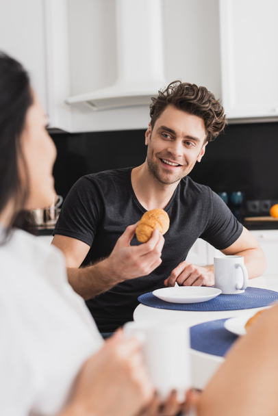 Selective focus of handsome man smiling at girlfriend with cup of coffee during breakfast in kitchen  - 写真・画像