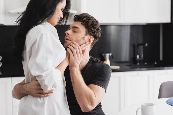 Handsome man embracing attractive girlfriend in kitchen  - Valokuva, kuva