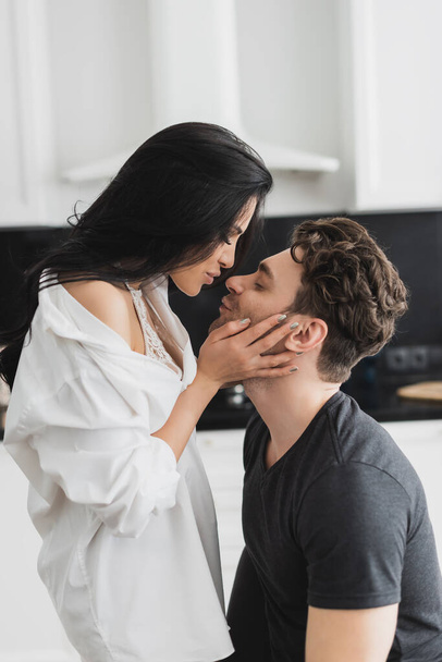 Side view of sexy woman in shirt kissing handsome boyfriend at home  - Zdjęcie, obraz