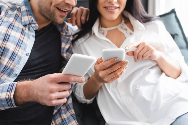 Cropped view of smiling woman pointing with finger at smartphone near boyfriend  - Foto, Imagen