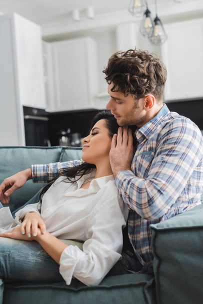 Selective focus of handsome man touching hair of attractive girlfriend on sofa  - Photo, Image