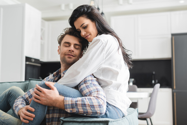 Beautiful woman hugging handsome man on couch in living room - Foto, imagen
