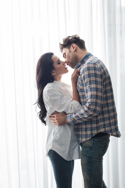 Handsome man kissing beautiful woman near window at home  - Photo, Image