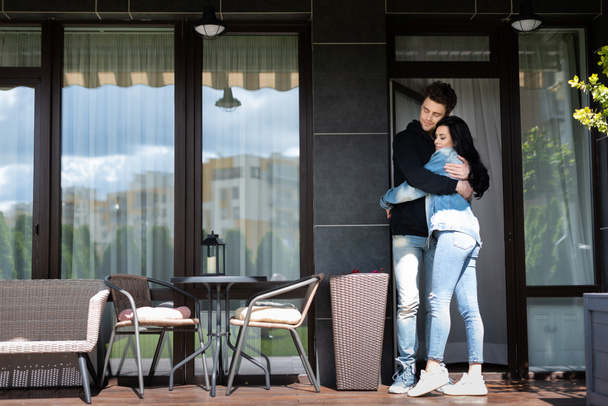 Young couple hugging on terrace near house at daytime - 写真・画像