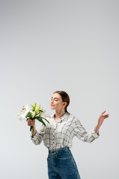 pleased attractive girl posing like puppet with flowers isolated on grey - Фото, зображення