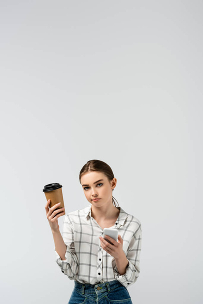 skeptical girl with smartphone and coffee to go isolated on grey - Fotó, kép