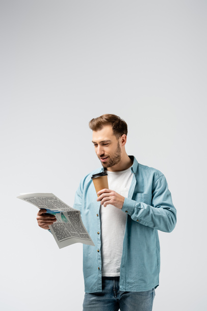 νεαρός άνδρας διαβάζει εφημερίδα και πίνει καφέ απομονωμένος στο γκρι - Φωτογραφία, εικόνα