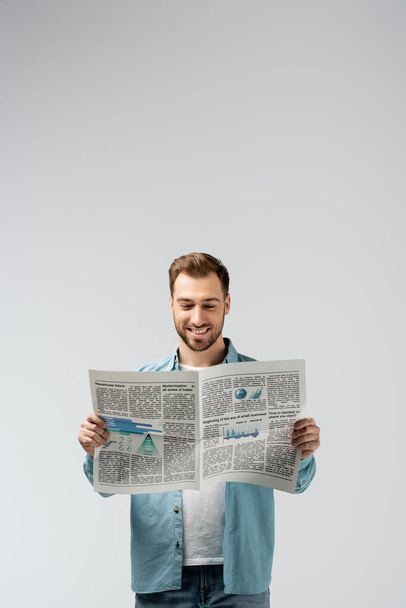 sonriente joven leyendo periódico aislado en gris
 - Foto, Imagen