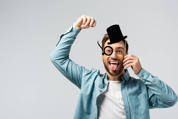 funny young man with fake hat and Pince-nez showing tongue isolated on grey - 写真・画像
