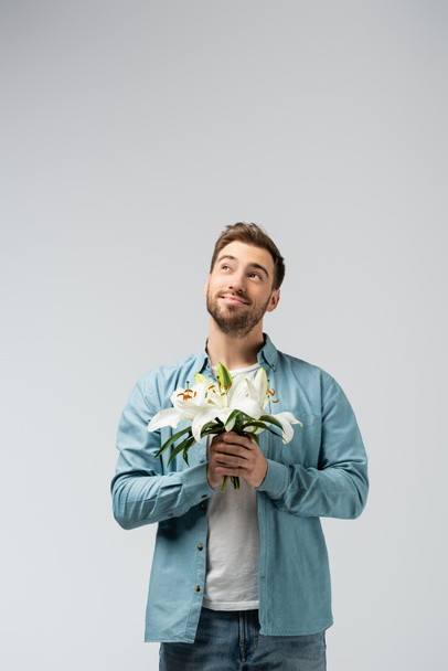 giovane uomo sognante con bouquet floreale isolato su grigio - Foto, immagini