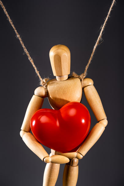 close up view of wooden marionette on strings with red heart isolated on black - Photo, Image