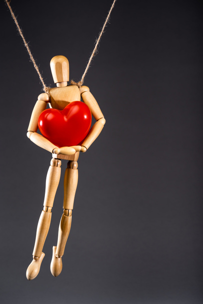 wooden marionette on strings with red heart isolated on black - Foto, Bild
