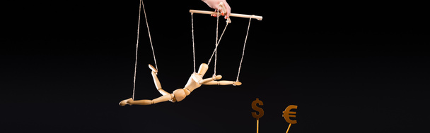vista ritagliata di burattinaio che tiene marionetta di legno su corde vicino a segni di valuta isolati su colpo nero, panoramico - Foto, immagini