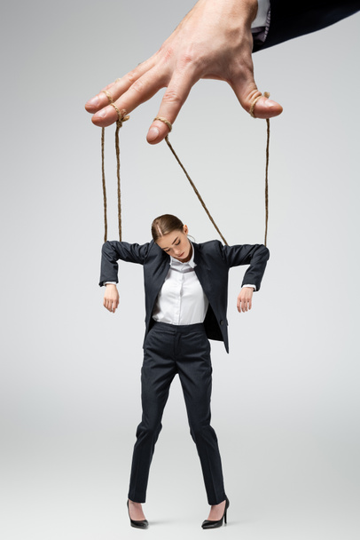 cropped view of puppeteer holding businesswoman marionette on strings isolated on grey - 写真・画像