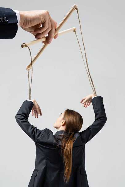 cropped view of puppeteer holding businesswoman marionette on strings isolated on grey - Fotografie, Obrázek