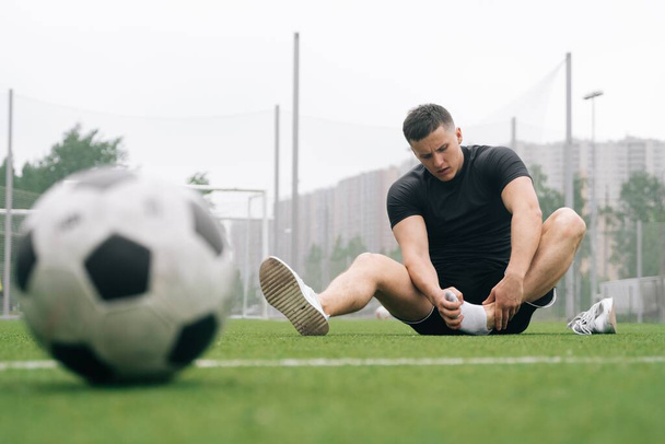 soccer player A man holds his foot. focus on the soccer ball. Dislocation or sprain of the joint. The concept of falling during sports. Break your leg in training - Foto, afbeelding