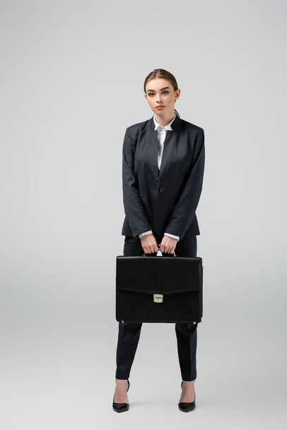 young businesswoman with leather suitcase isolated on grey - Foto, afbeelding