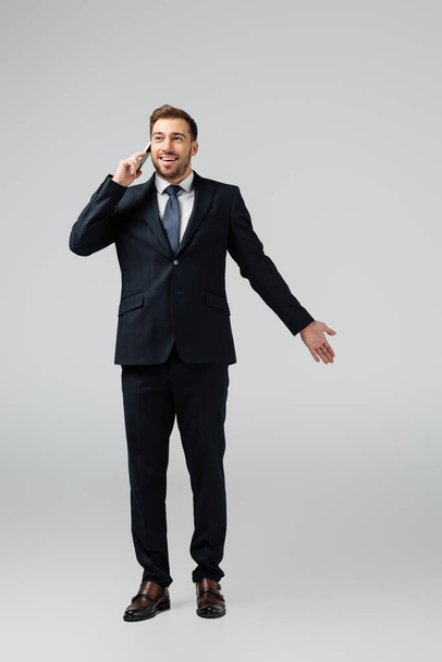 smiling handsome businessman in suit talking on smartphone isolated on grey - Photo, Image