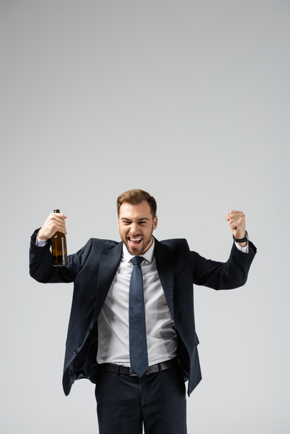 handsome businessman in suit rejoicing with beer isolated on grey - Valokuva, kuva