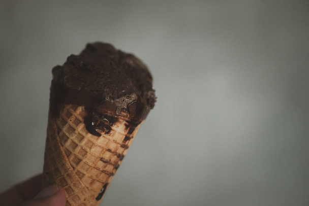 Ugryzienie czekoladowego wafelka lodowego w dłoni. Słodkie menu koncepcja. - Zdjęcie, obraz