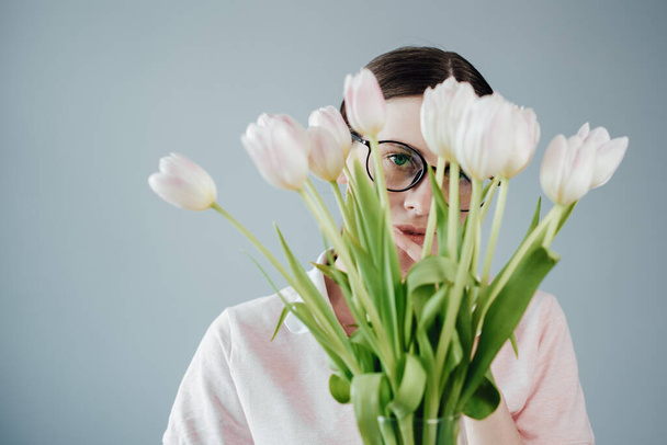 Studio Portrait of Young Adult Pretty Girl con gafas vestidas con camiseta rosa sostiene un ramo de tulipanes frescos
 - Foto, Imagen