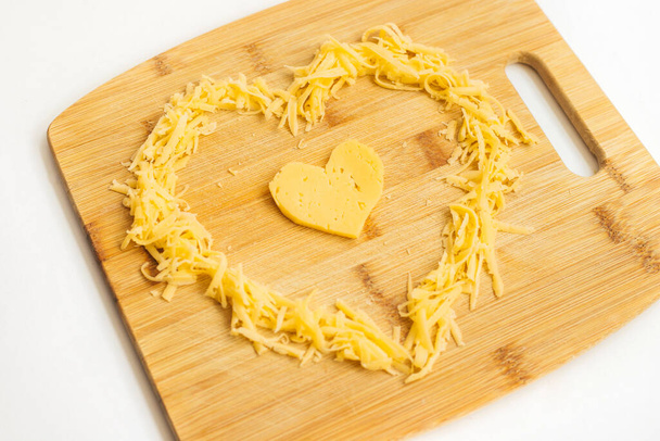 Cheese in the shape of a heart on a wooden Board. Grated cheese in the shape of a heart. Hard cheese.Cheese is for lovers. - Fotoğraf, Görsel