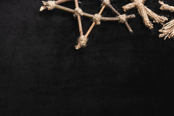bovenaanzicht van voodoo pop bij pentagram met houten stokjes op zwart - Foto, afbeelding