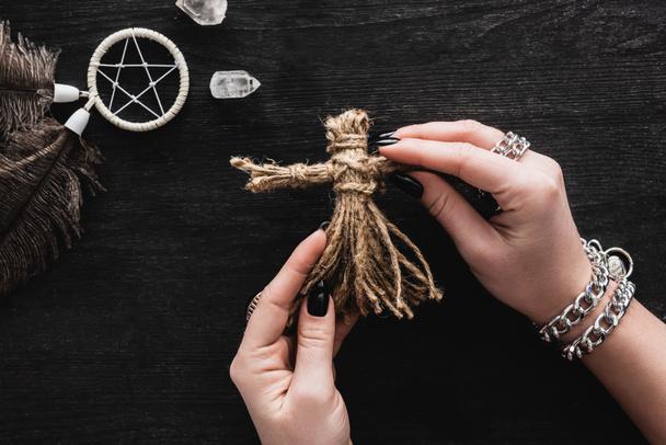 top view of woman holding voodoo doll in hands near pentagram and crystals on black  - Fotó, kép
