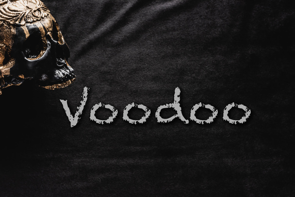 Okkulter Schädel in der Nähe von Voodoo-Schriftzug auf Schwarz  - Foto, Bild