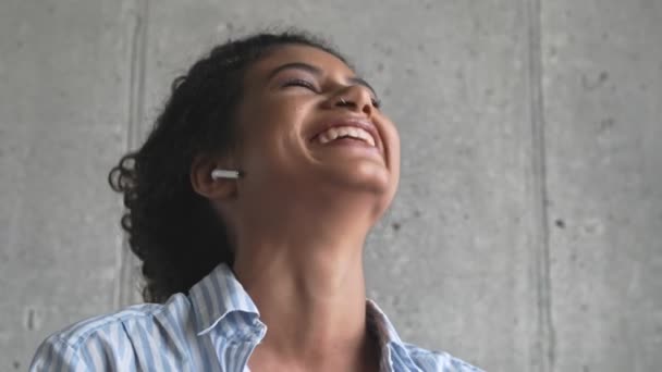 Een vrolijke jonge Afrikaanse vrouw met oordopjes zit thuis in de woonkamer te bellen. - Video