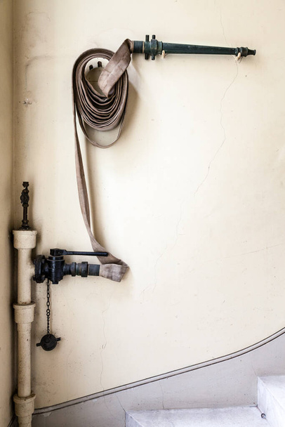 Alte Feuerwehrschläuche und -düsen hingen an einer Wand im Treppenhaus und waren mit einem Standrohr verbunden. Eine Form des Brandschutzes in vergangenen Zeiten. - Foto, Bild