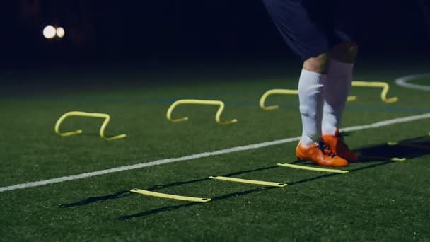 Trainingstoestellen voor behendigheid van voetbal. Professionele voetballer met behendigheidsladder en horden 's nachts, 4k slow motion - Video