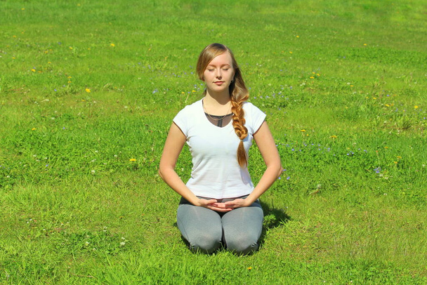 Jonge vrouw van Europese verschijning doet yoga in de zomernatuur. Vrouw in heldenhouding, Virasana. Hoge kwaliteit foto voor web en print met lege ruimte voor tekst en design. - Foto, afbeelding