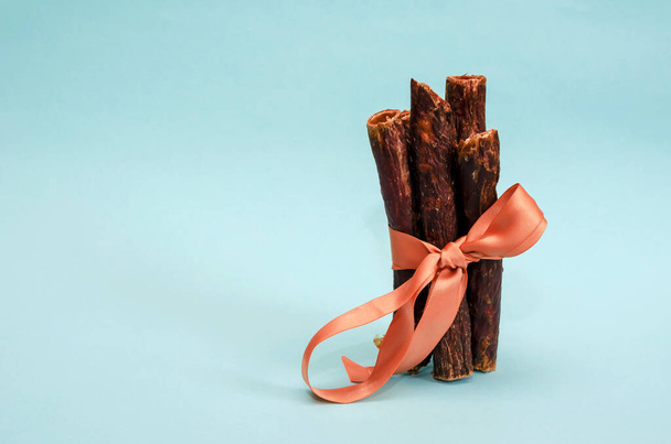 Sticks of dried beef esophagus on a turquoise background. Natural healthy treats for pets. Beef sticks for dogs tied with a ribbon. Pet supplies. - Photo, Image