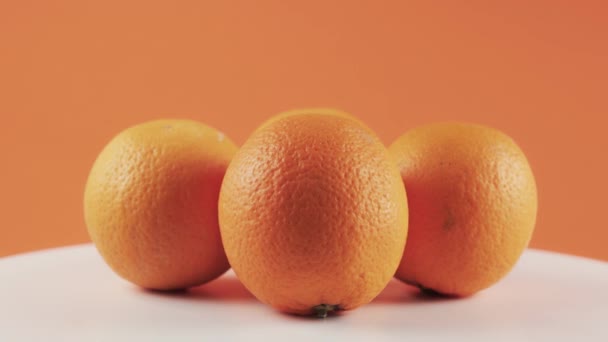 Close up, four oranges on white spinning table isolated on orange background - Video