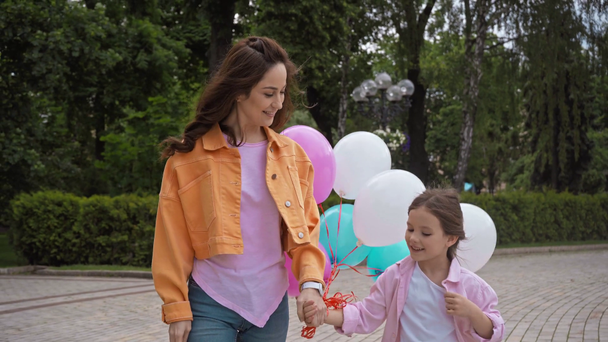 χαριτωμένο παιδί μιλάμε και κρατώντας το χέρι με τη μητέρα κοντά μπαλόνια στο πάρκο - Πλάνα, βίντεο