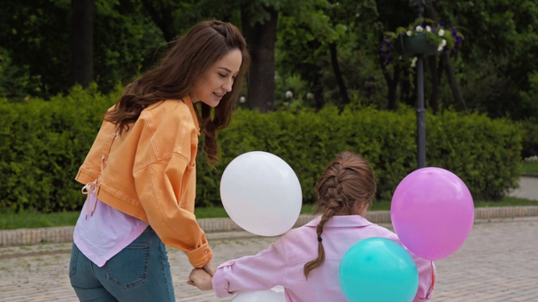 mother holding hands with daughter and walking with balloons in park - Footage, Video