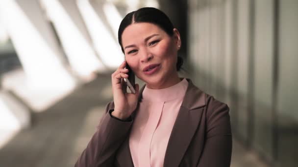 Asian business woman talking on the phone standing outdoors near office building. Beautiful woman having conversation on the phone with colleague. Business concept. Toned footage. Prores 422 - Imágenes, Vídeo