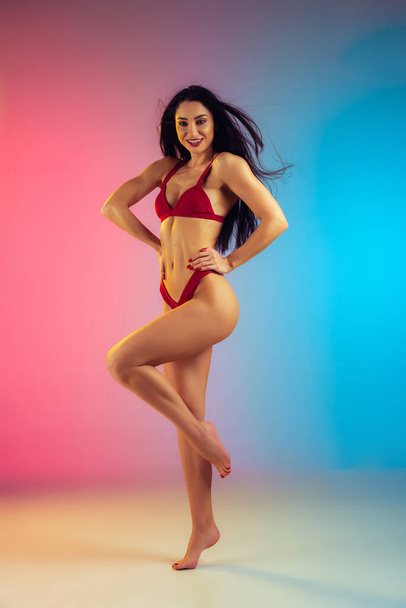 Fashion portrait of young fit and sportive woman in stylish red luxury swimwear on gradient background. Perfect body ready for summertime. - Fotoğraf, Görsel