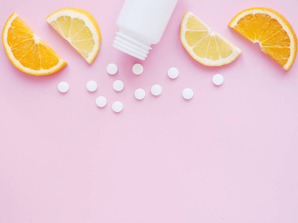 scattered vitamin pills from bottle with lemon and orange on pink background. Copyspace, flat lay. Concept boost immune system, medicine and tablets - Foto, imagen