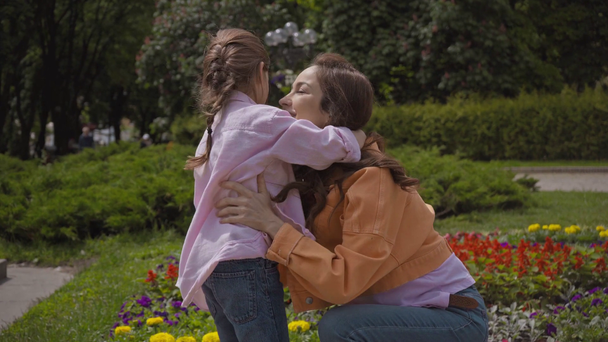 mother and daughter shaking hands and hugging near flowerbed outside - Footage, Video