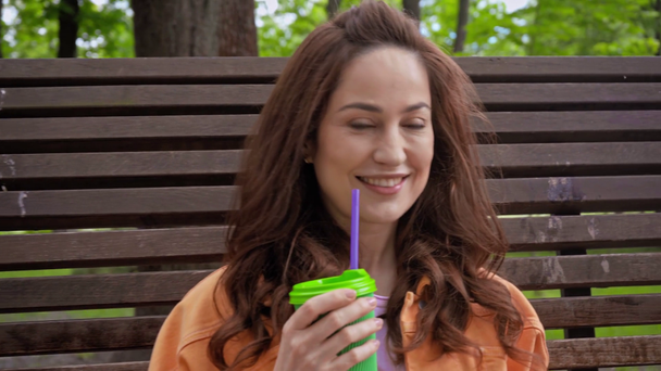 happy woman drinking coffee to go through straw in park  - Materiał filmowy, wideo