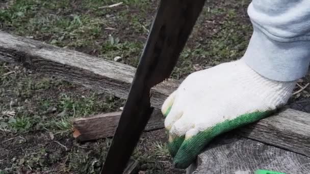 Een arbeider in handschoenen zaagt planken met een handzaag. Zijaanzicht. Gereedschap voor huishoudelijk gebruik zonder elektriciteit. - Video