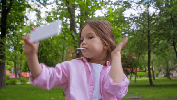 παιδί με γλειφιτζούρι βγάζει selfie και δείχνει την πινακίδα ειρήνης στο πάρκο  - Πλάνα, βίντεο
