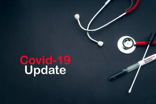 COVID-19 UPDATE Text mit Stethoskop und medizinischen Abstrichen auf schwarzem Hintergrund. Covid -19 oder Coronavirus-Konzept  - Foto, Bild