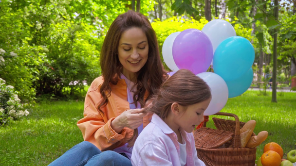 Mutter singt mit süßer Tochter und flechtet Zopf im Park  - Filmmaterial, Video